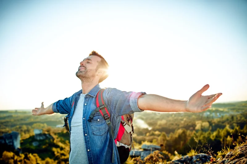 Smiling man extending arms while hiking in beautiful hills